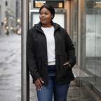 HHE plus size women's puffer jacket in classic black, practical and comfortable everyday wear, worn outdoors strolling by a stone building.